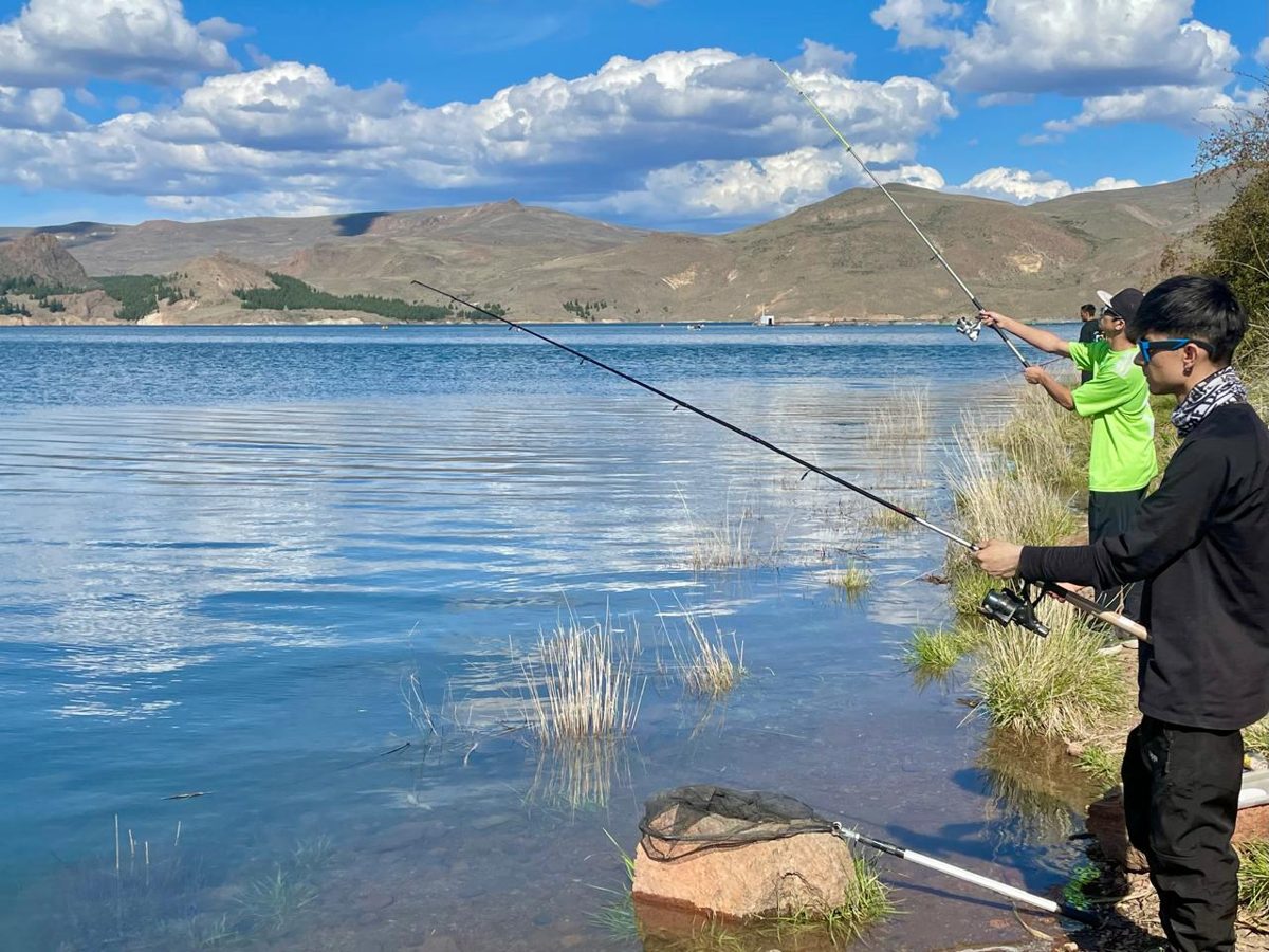 Tres personas pescando con spinning desde la orilla del Embalse Alicurá